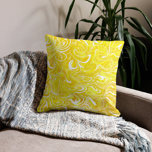 An 22x22-inch decorative throw pillow featuring abstract yellow and white swirling patterns inspired by original artwork. The pillow rests on a beige armchair draped with a textured, neutral-colored blanket, with green houseplants in the background adding a cozy, modern home aesthetic.