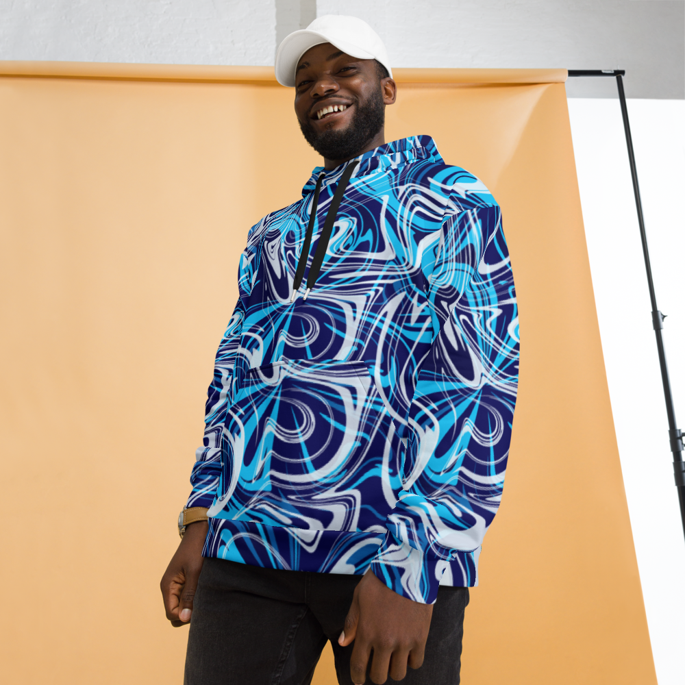A man smiling while wearing a vibrant blue, white, and navy abstract swirl patterned hoodie. The hoodie features a relaxed fit with a front pocket and black drawstrings. The bold, fluid design creates a dynamic, artistic look. He is posing in front of a peach-colored studio backdrop while wearing a white cap and dark pants. 